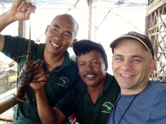 Three men are facing the camera smiling holding a lobster.