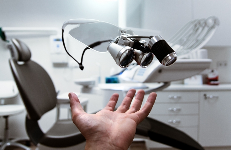 A chair and a large machine used by optometrists sits in the background. A hand is reaching towards the equipment in the foreground.