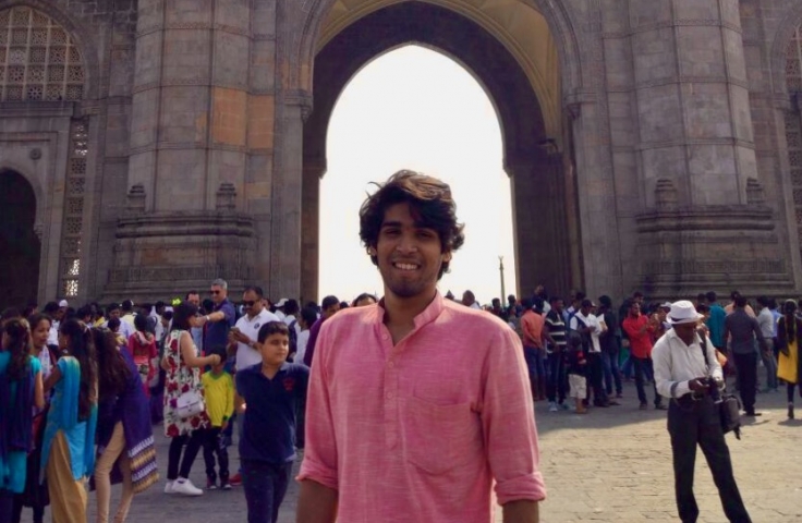 Akhil stands in the foreground with people behind him in front of a large historical archway.
