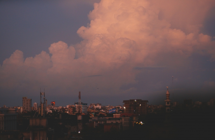 Image of cityscape at sunset with large fluffy clouds. Clouds are tinted pink by sunset.