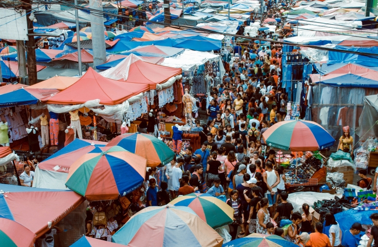 Image of informal market with stalls covered by tents. Crowds of people are walking between the tents.