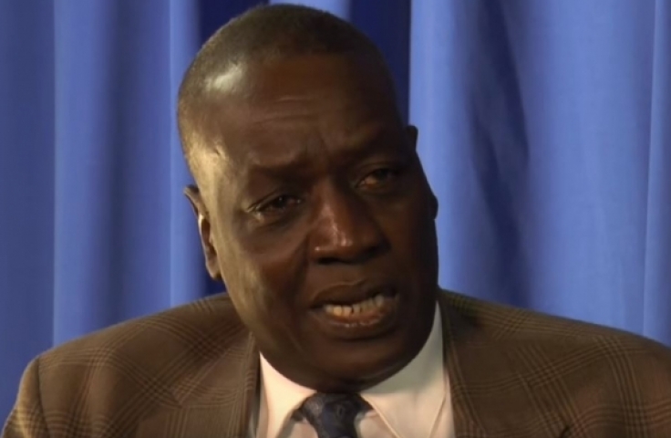An image of Dr Luka Biong Deng Kuol speaking to the camera in front of a blue curtain.
