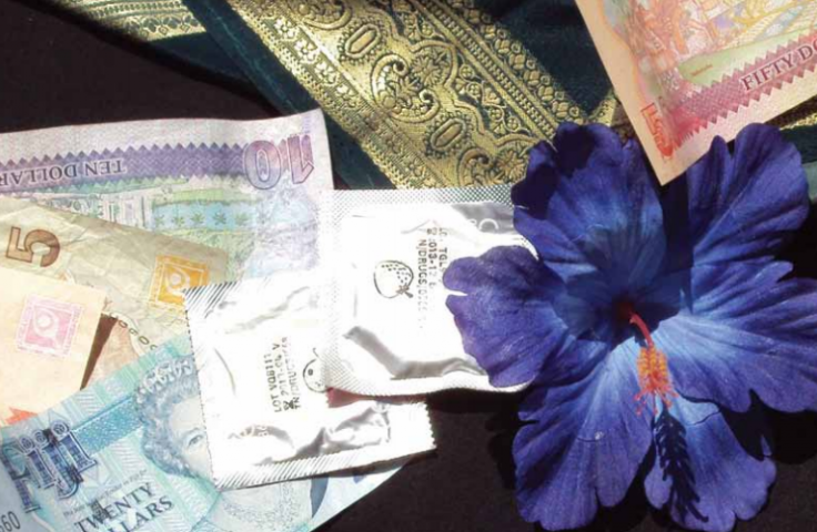 In this image, currency notes, condoms and a hibsicus flower are laid out on the table.