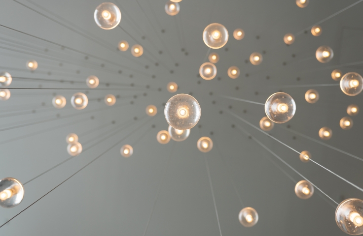 Lightbulbs are suspended from a ceiling. The photograph captures a low profile view of the bulbs from underneath. 