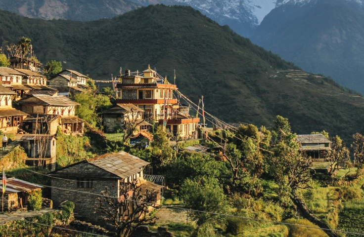 A landscape shot of Nepal shows homes on a hillside in the foreground and ice capped mountains in the distance.