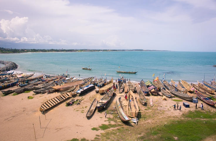 A landscape shot of a coast line. On the beach in the foreground are small canoe-like boats.