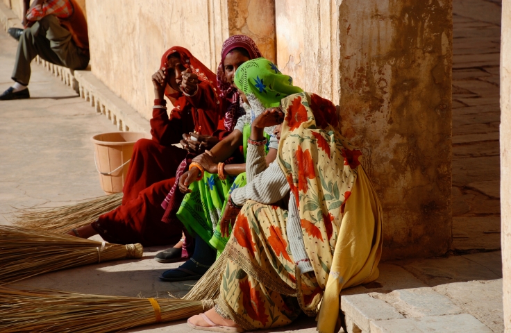 Women sit in the street in India. They are facing away from the camera.
