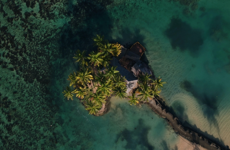 This is an aerial shot of a small, tree covered island in the middle of the ocean.