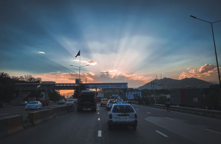 This image shows a road in Kabul as the sun rises. There are cars in the foreground travelling towards a bridge in the background.