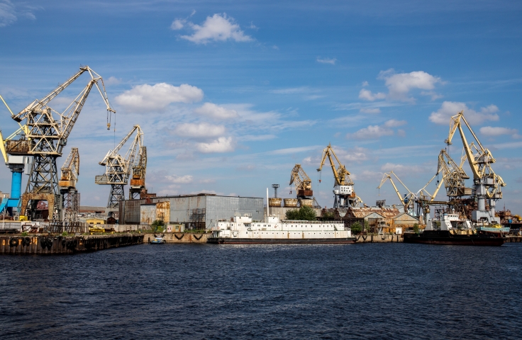 This image shows a ship in the water, amongst a port with various cranes.